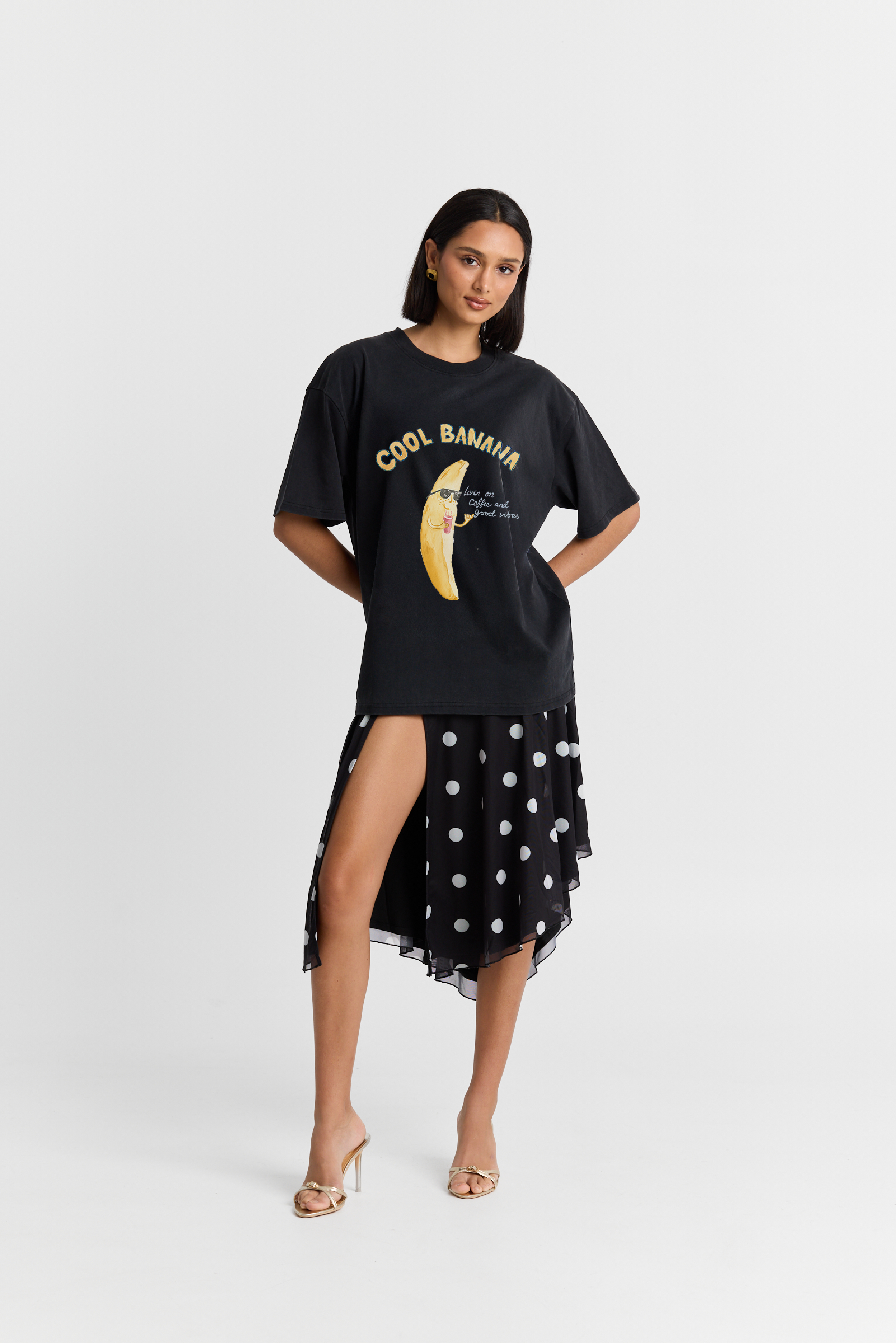 Woman wearing a black oversized t-shirt with a graphic design and a black polka dot skirt on a white background