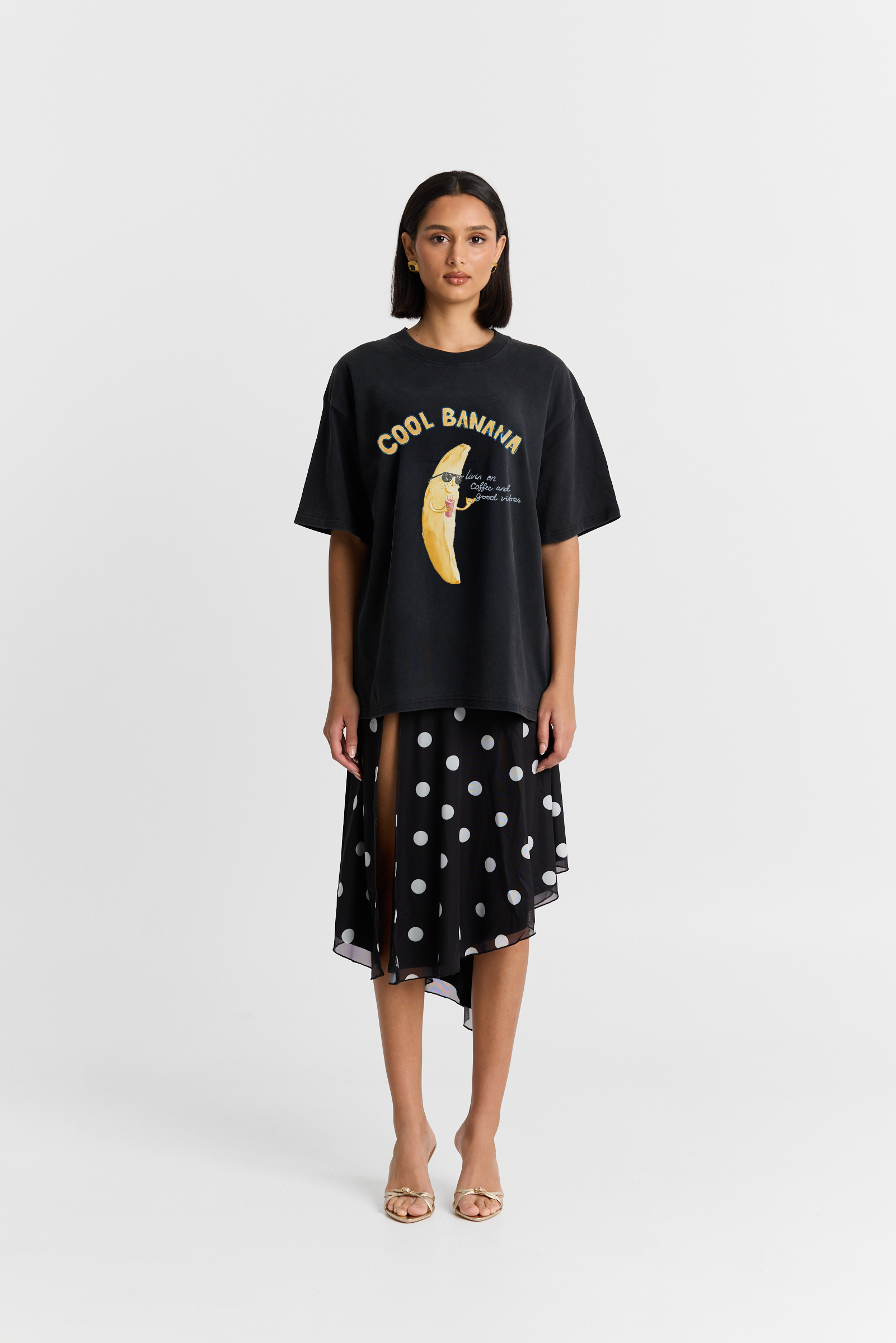 Woman wearing a black t-shirt with 'Cool Banana' graphic and a black polka dot skirt on a white background