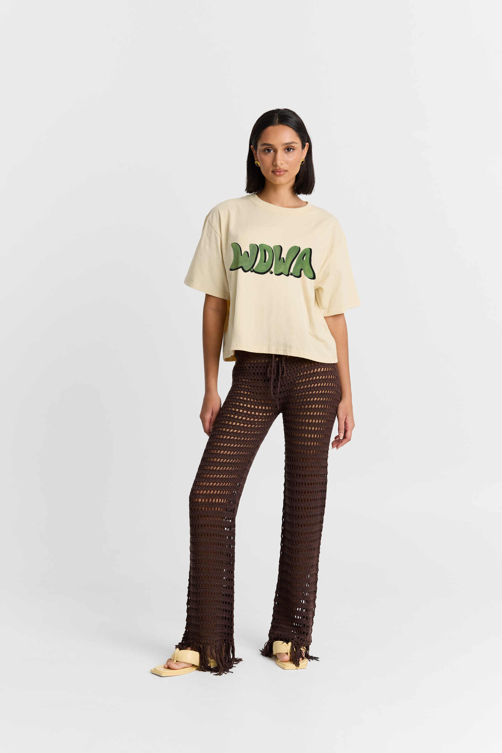 Woman wearing a beige t-shirt with green text and brown pants on a white background