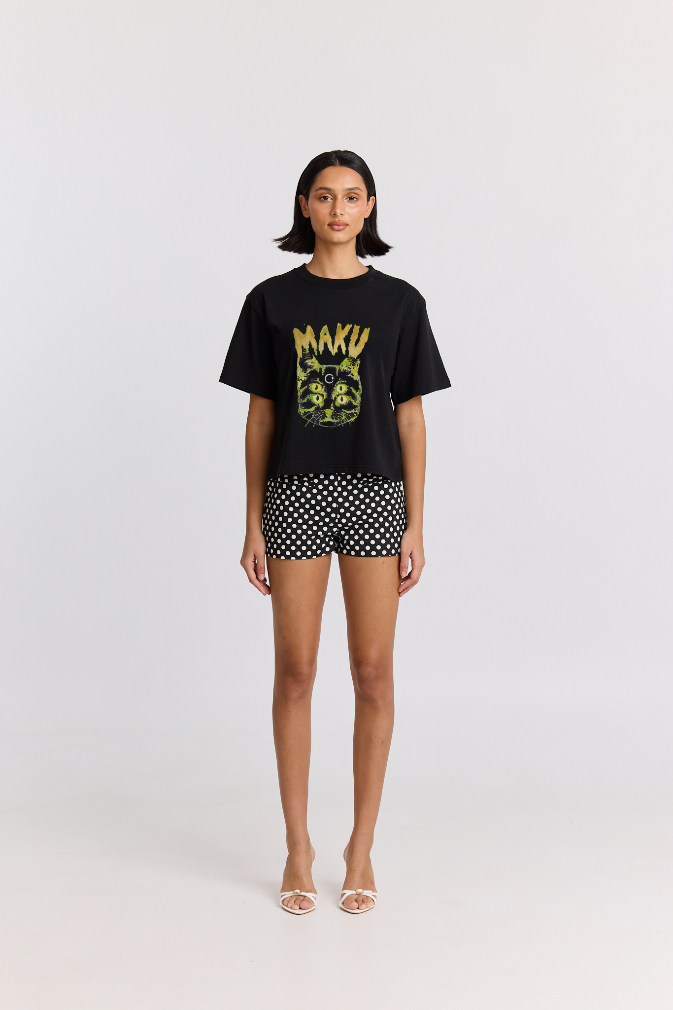 Person wearing a black t-shirt with a CAT design and polka dot shorts on a white background